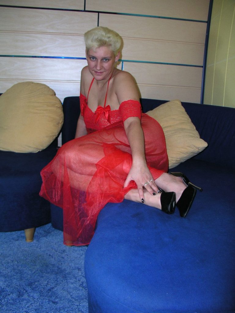 Kurhaarige blonde MILF in roter Reizwäsche wartet auf dem Bett